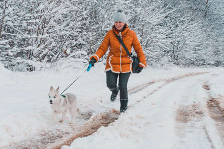 Beautiful woman in orange jacket with husky puppy running through forest road.2020の写真素材