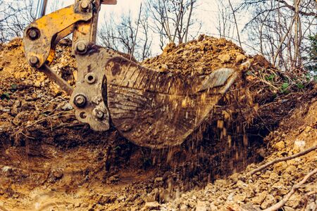 Backdrop of excavator bucket with soil on forest and sky background.2020