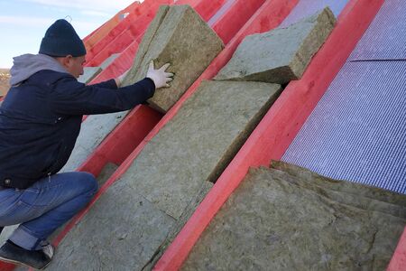 The worker puts mineral wool on the roof, insulating the house.2020