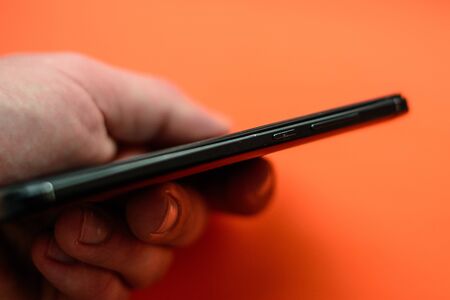 Man's hand holds smartphone and shows its side parts. 2020