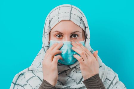 Woman in white scarf and puts mask on face on blue background.2020