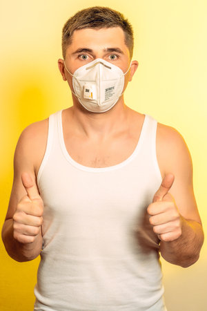 Wuhan, China - April 21 2020: Patient man in medical mask on self isolation during quarantine and coronavirus pandemic stands with arms crossed new. Shows a thumbs-up of both hands.のeditorial素材