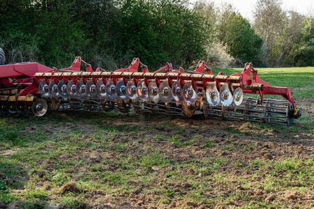A red modern harrow stands in a field before sowing. Hydraulic mechanism for grinding the soil after plowing.の写真素材