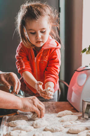 little grandmother's granddaughter learns to cook, sculpt dumplings. on the table are stuffing for dumplings, dough, meat grinder. home cuisine 2020の写真素材