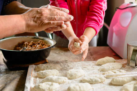 little grandmother's granddaughter learns to cook, sculpt dumplings. on the table are stuffing for dumplings, dough, meat grinder. home cuisine 2020の写真素材