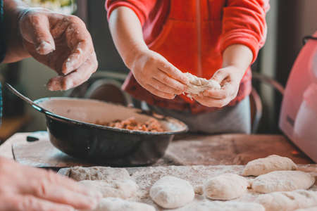 Grandmother and granddaughter sculpt dumplings with meat filling. On the table are flour, stuffing,...