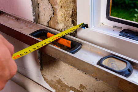 The man performs installation work with the window, for this he also uses a tape measure, measures...