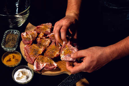 Marinating pork neck skewers, adding salt, curry and basil to the meat, pieces of meat on a wooden...