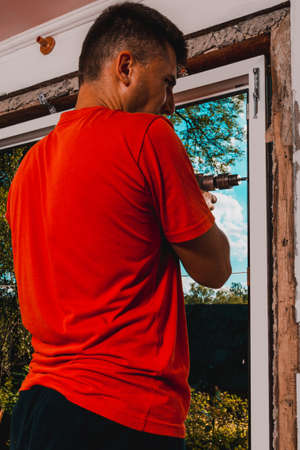 A man in his own house installs a plastic window, installs a new window, a worker uses an electric...