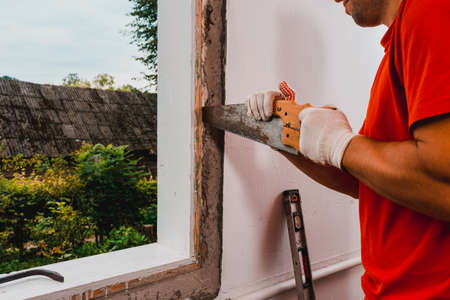 The man with a hand saw cuts the mounting wool around the window frame, installation of an old wooden window, window replacement. 2020の写真素材
