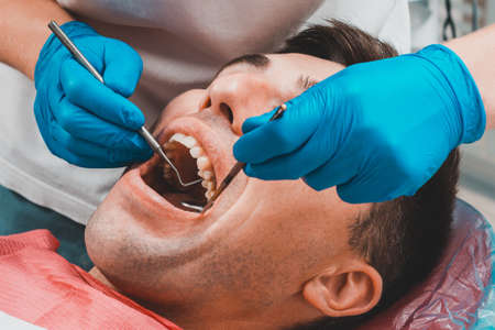 Dental clinic, the patient sits in a dental chair with his mouth wide open, the dentist assesses the condition of the teeth and makes a diagnosis. 2020の写真素材