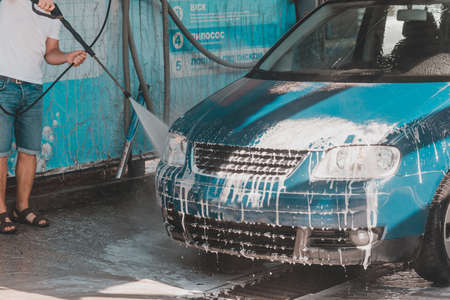 Self-service car wash, a person washes the foam from the car with water under high pressure. 2020