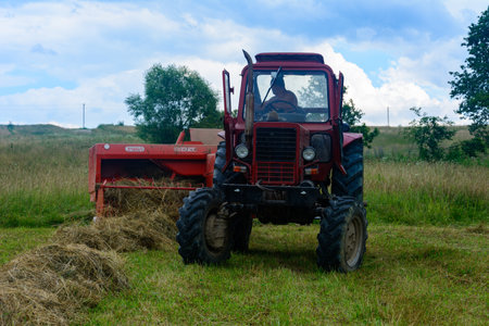 Dolyna, Ukraine July 11, 2020: Belarus tractor in the field, bale of hay, summer time, forage harvesting for cattle. 2021のeditorial素材