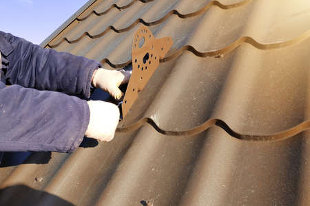 The worker works at height, attaches snow-cutting elements to the galvanized roof, work in the cold...