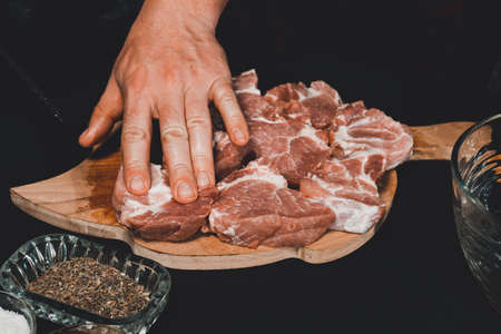 A man on a wooden board cuts pork into large pieces, close-up shows how to cut pork neck on a barbecue. 2020の写真素材