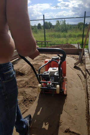 The worker controls the vibrating plate at the construction site, heavy manual construction equipment, pressing and compaction of sand. newの写真素材