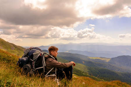 A young tourist sits on a background of mountains with a backpack, relaxing and admiring the views of the Carpathians in Ukraine.2020の写真素材