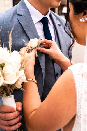 The bride puts a boutonniere on the groom's jacket on their wedding new day.