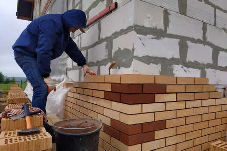The worker walls the walls of the house with red brick facade, the process of building a new...