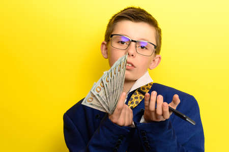 Successful and rich child taking a selfie with money, portrait of a boy in a suit on a yellow background. newの写真素材