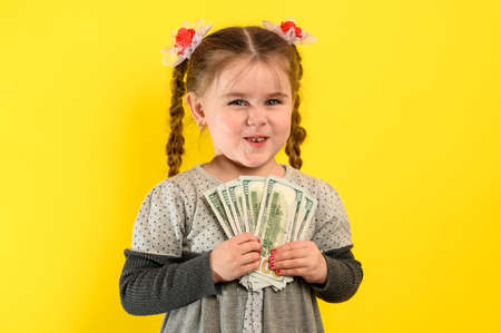 Children and financial responsibility, little girl on a yellow background with dollars in her hands, financial literacy in a child. newの写真素材