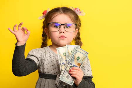 Money and children on the background, a rich girl with glasses holding a large sum of money.の写真素材