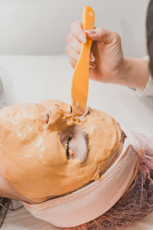 spa treatments in a beauty salon, hand of a professional beautician applying a gold mask on the...