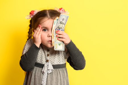 Caucasian girl holding money, portrait of a child on a yellow background, financial literacy of children. newの写真素材