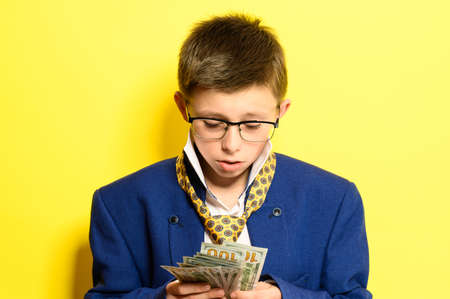 Boy in an adult suit on a yellow background, international currency in the hands of a child, children's savings for the future. newの写真素材