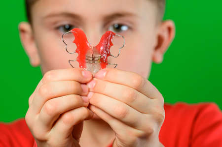 A boy on a green background shows his plate for aligning teeth. new