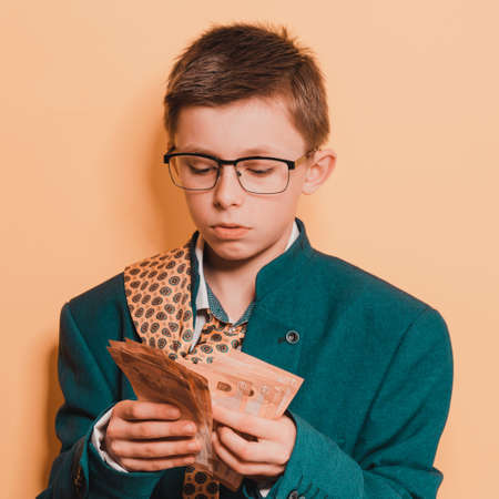 An 11-year-old boy in an adult and oversized suit holds a euro, a portrait of a child with money on...