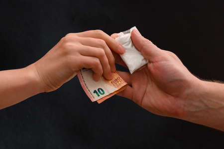 Drug dealer passes a dose to a merchant, sachets of powder on a black background.の写真素材