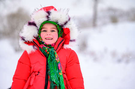 A happy girl in a red jacket and Ukrainian national kerchief walks in a snowy yard. newの写真素材