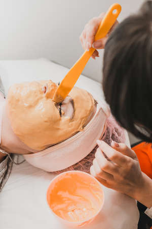 spa treatments in a beauty salon, hand of a professional beautician applying a gold mask on the client's face. newの写真素材