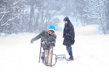 Two boys carry sledges on their shoulders to ride them down the slide, children and winter, children's entertainment.の写真素材