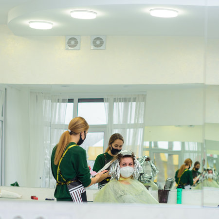Dolyna, Ivano-Frankivsk March 5, 2021: Pandemic and the work of hairdressers, stylist and client during the procedure of dyeing in medical masks, hair bleaching.のeditorial素材