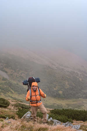 A man climbs a mountain in the fog, a man carries a backpack on his back, a tourist trip with an...