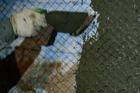 The master throws a solution of liquid concrete on the wall, the first layer of plaster on the wall, metal mesh attached to a wooden wall.の写真素材