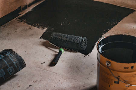 Applying hot resin to the floor for waterproofing, roller and bucket of resin, black and liquid resin.の写真素材
