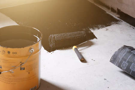 Applying hot resin to the floor for waterproofing, roller and bucket of resin, black and liquid resin.の写真素材