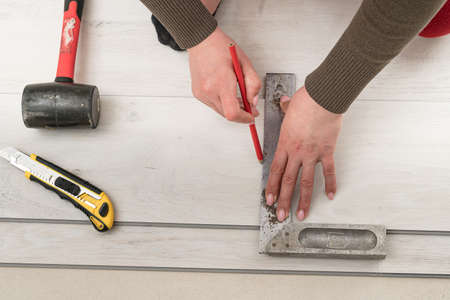 Female master draws a pencil line on the board, installing quartz vinyl flooring, installation work.