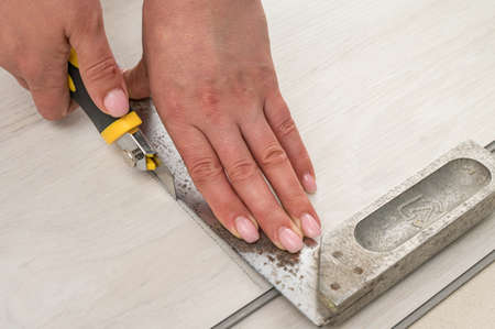 Female master cuts quartz vinyl floor with a stationery knife, floor installation, woman performs repair work.の写真素材