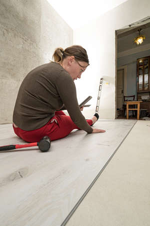 Installing a quartz vinyl floor, a woman performs installation work, installing a floor with a hammer and angle.の写真素材