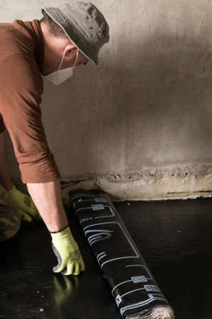The worker untwists the roll of waterproofing and fastens it to the resin, installing waterproofing.の写真素材