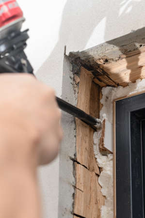 a man uses a spray gun with his hand and fills the gap with construction foam between a new wooden...