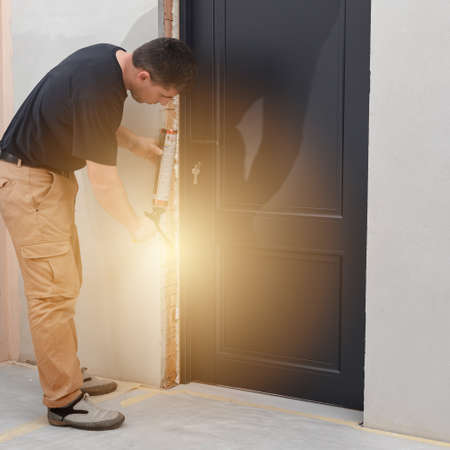 a man uses a spray gun with his hand and fills the gap with construction foam between a new wooden door and a wall, the process of installing a door.の写真素材