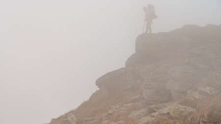 A man with a backpack for a hike climbs to the top of the mountain on a rocky path, a tourist hike in the Carpathians in Ukraine, a tourist in the fog.の写真素材