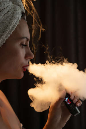 The girl emits smoke from a vape, a portrait of a girl with red lips who smokes on a black...