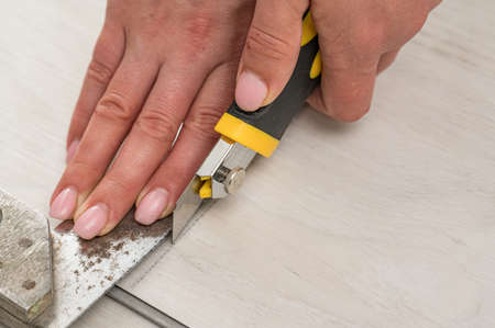 Female master cuts quartz vinyl floor with a stationery knife, floor installation, woman performs...