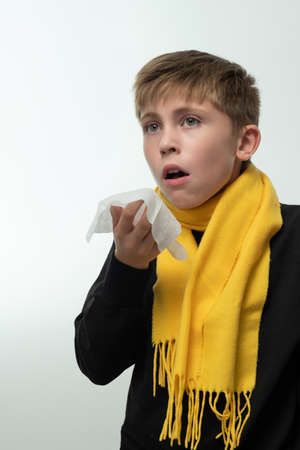 The child sneezes into a handkerchief, symptoms of colds, the boy is wrapped in a yellow scarf.の写真素材